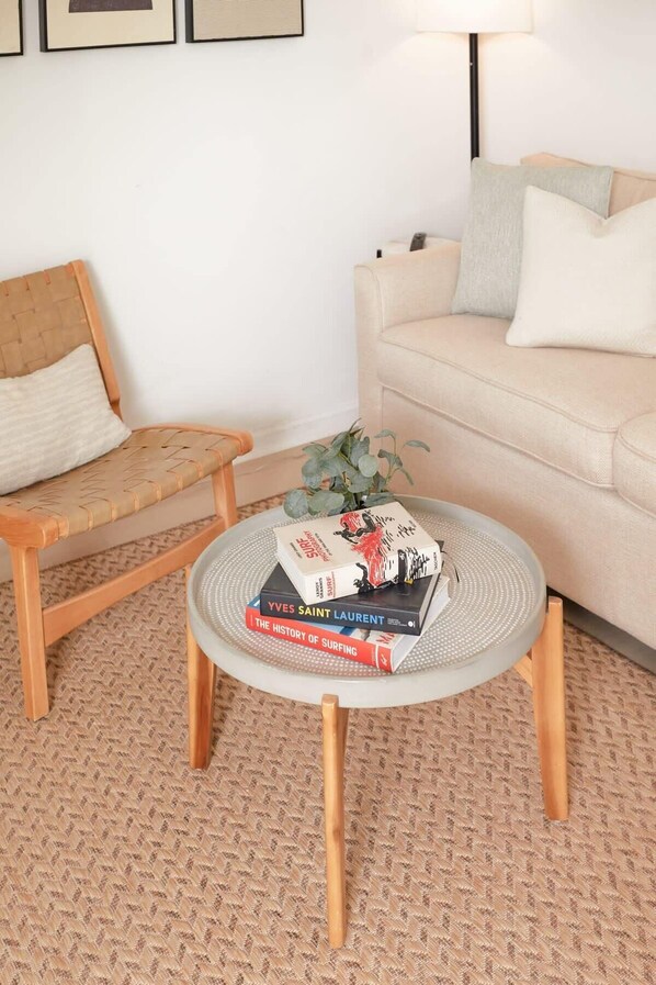 Una sala de estar con un sofá color beige, una silla de madera y una mesa de centro redonda con libros.