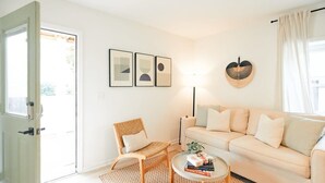Una sala de estar con un sofá, una butaca, una mesa de centro y una puerta que da a un espacio exterior.