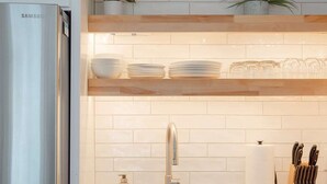 A modern kitchen with white cabinetry, a stainless steel refrigerator, a sink with a modern faucet, and a countertop with a knife block and a potted plant.