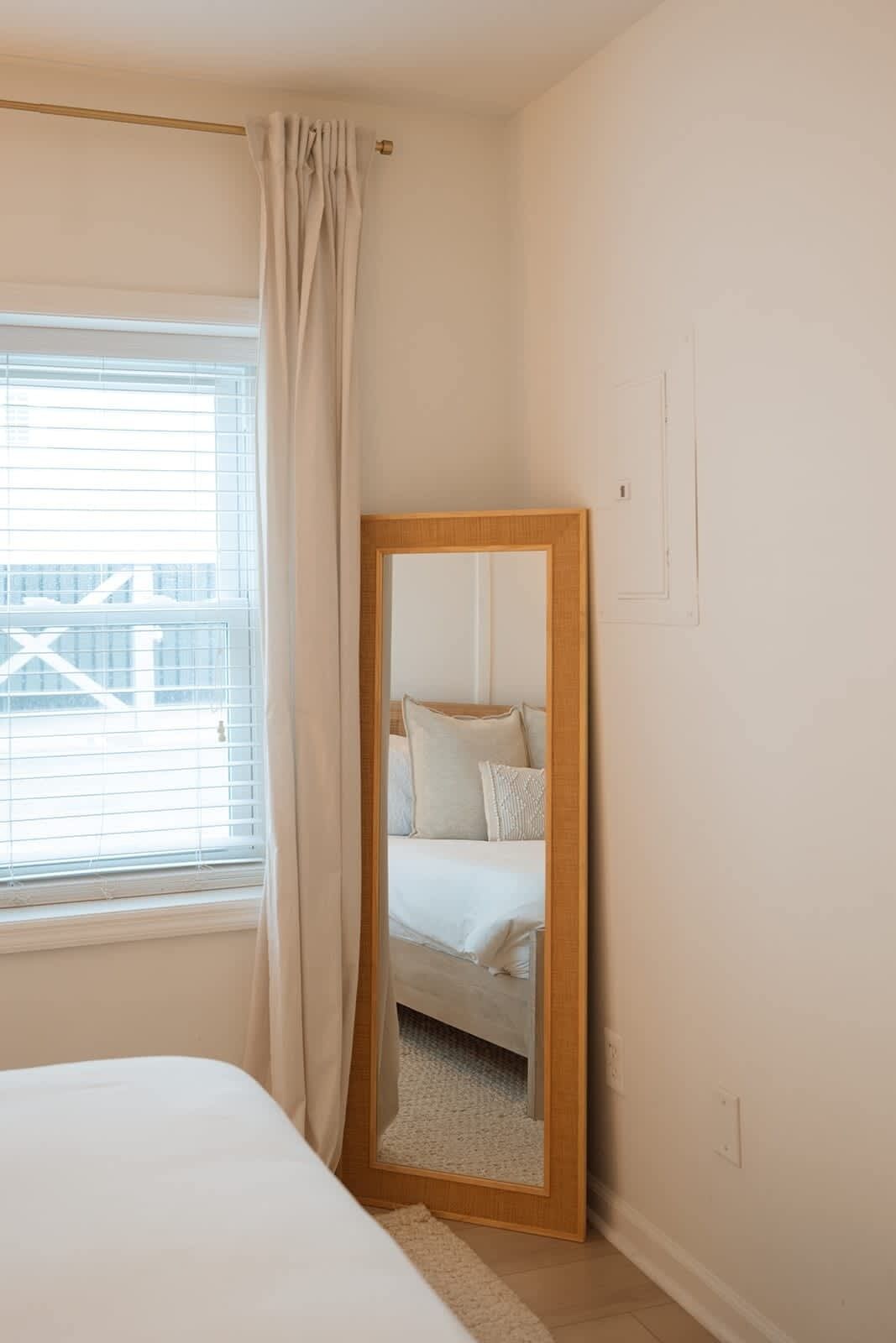 A bedroom with a bed, a large mirror, a window with blinds, and a curtain.