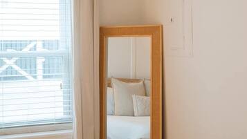 A bedroom with a bed, a large mirror, a window with blinds, and a curtain.