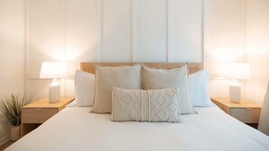 A neatly made bed with four pillows, two bedside tables with lamps, and a wooden headboard.