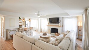 A modern living room with a sofa set, a fireplace, a TV mounted above it, and a dining area with a table and chairs.
