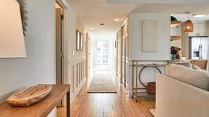 A hallway leading to a kitchen with wooden flooring, a sofa, and a dining table.