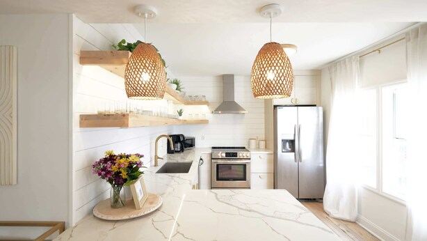 A modern kitchen with white marble countertops, stainless steel appliances, and wicker pendant lights.