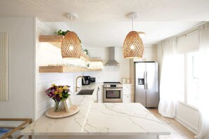 Una cocina moderna con encimeras de mármol blanco, electrodomésticos de acero inoxidable y lámparas colgantes de mimbre.
