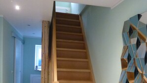 Un escalier en bois menant à l’étage supérieur, un mur bleu clair orné d’une étagère géométrique et un radiateur à l’arrière-plan.
