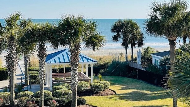 Un gazebo dal tetto blu, circondato da palme e prati curati, con vista su una spiaggia.