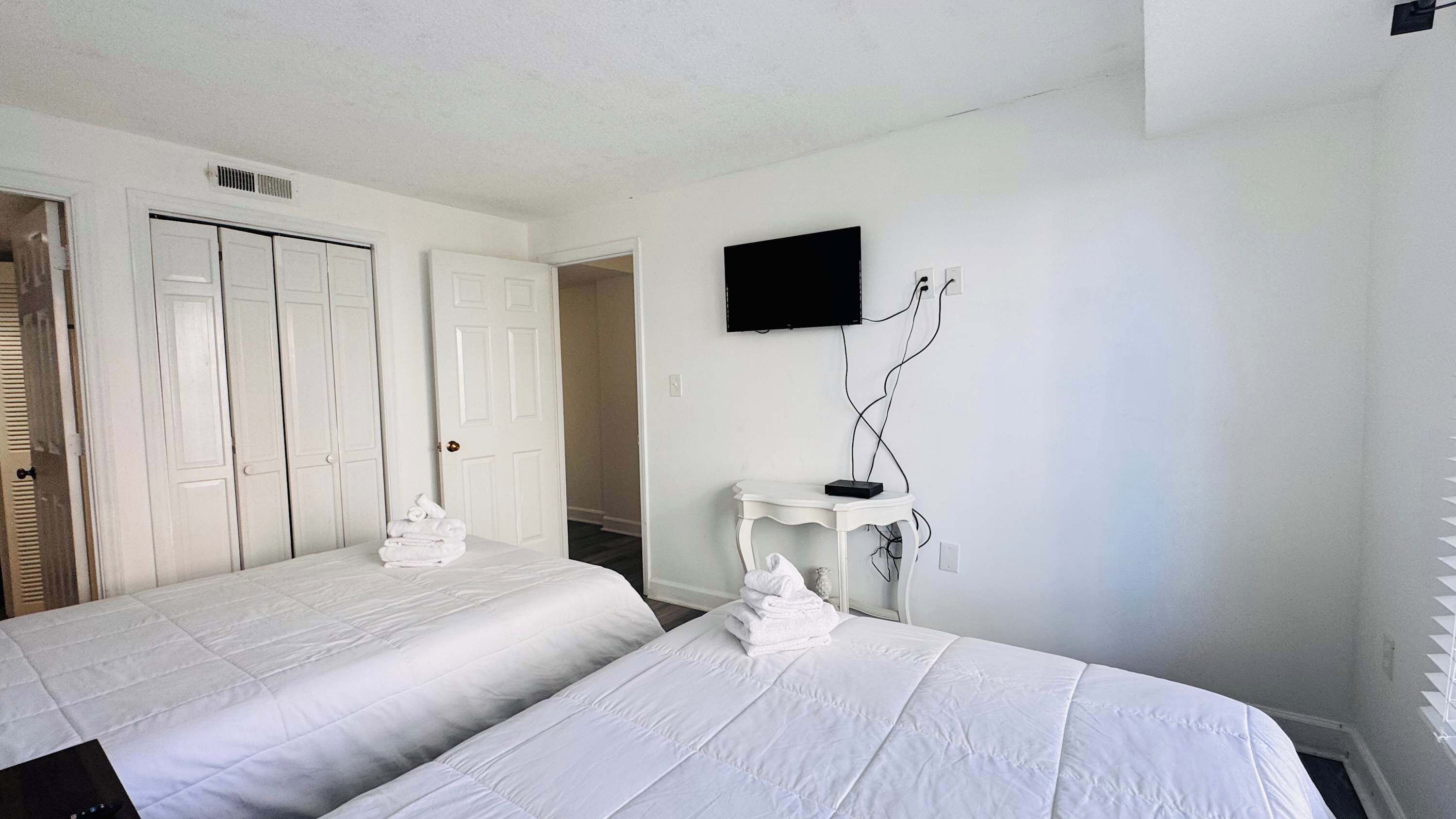 A hotel room with two beds, a TV mounted on the wall, and a small table with a lamp.