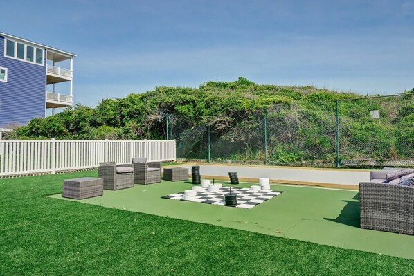 Une cour avec des sièges en plein air, une table à jeux à carreaux et un bâtiment en arrière-plan.