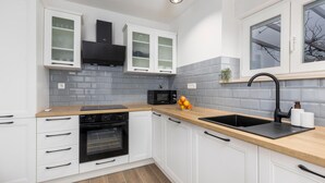 A modern kitchen with white cabinets, a black oven, a microwave, and a sink with a black faucet. - 4 bedroom lovely apartment in Cernik (Cernik)