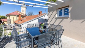 An outdoor patio with a table and chairs, a pergola with climbing plants, a view of a church with a bell tower, and a window on the building. - 4 bedroom lovely apartment in Cernik (Cernik)