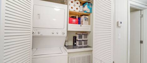 A laundry room with a washer and dryer, a shelf with toiletries, and a first aid kit.
