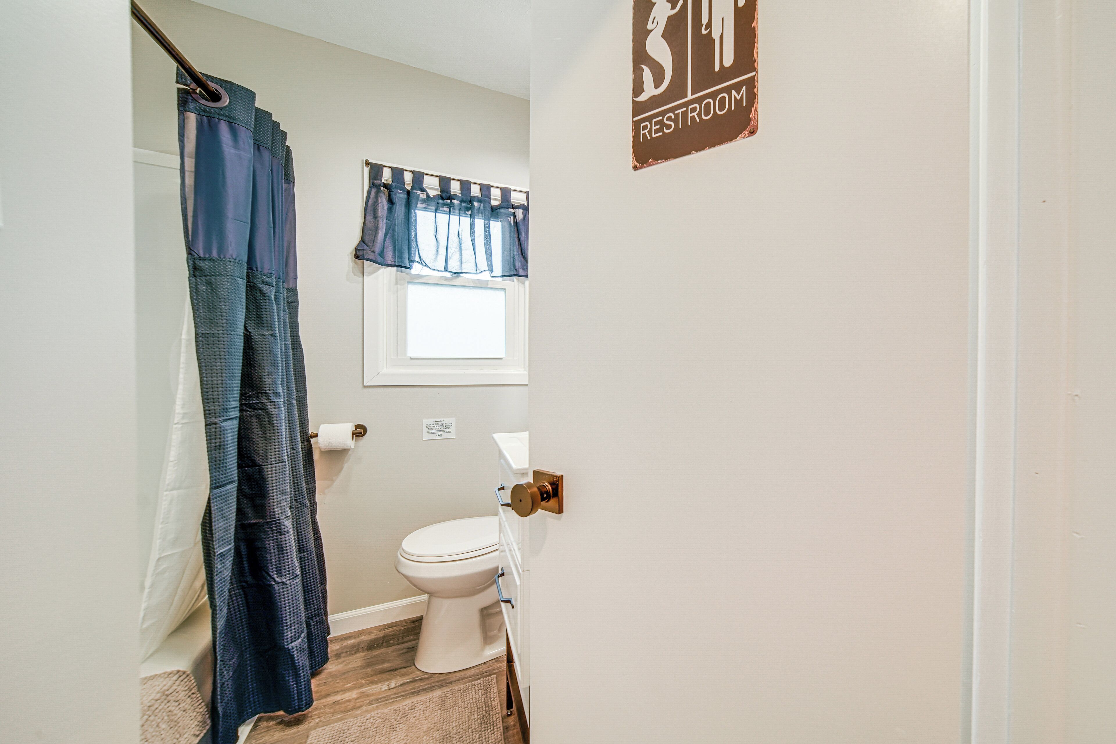 A bathroom with a toilet, a shower curtain, and a window.