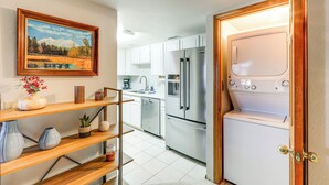 Une cuisine moderne avec des armoires blanches, des appareils en acier inoxydable et une étagère en bois agrémentée d’objets décoratifs.