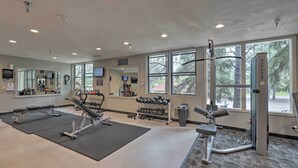 Une salle de sport équipée de divers appareils d’exercice, dotée de grandes fenêtres et d’un miroir.
