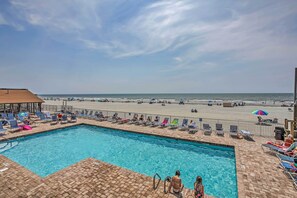 A pool with lounge chairs and umbrellas, a beach in the background, and a clear sky. - Oceanfront Gem w/ Community Perks in Myrtle Beach (Myrtle Beach)