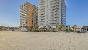 A beach with footprints leading to a building with multiple balconies and a sign indicating a parking area. - Oceanfront Gem w/ Community Perks in Myrtle Beach (Myrtle Beach)