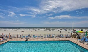 A pool area with clear blue water, a beach in the background, and a wooden deck with lounge chairs. - Oceanfront Gem w/ Community Perks in Myrtle Beach (Myrtle Beach)