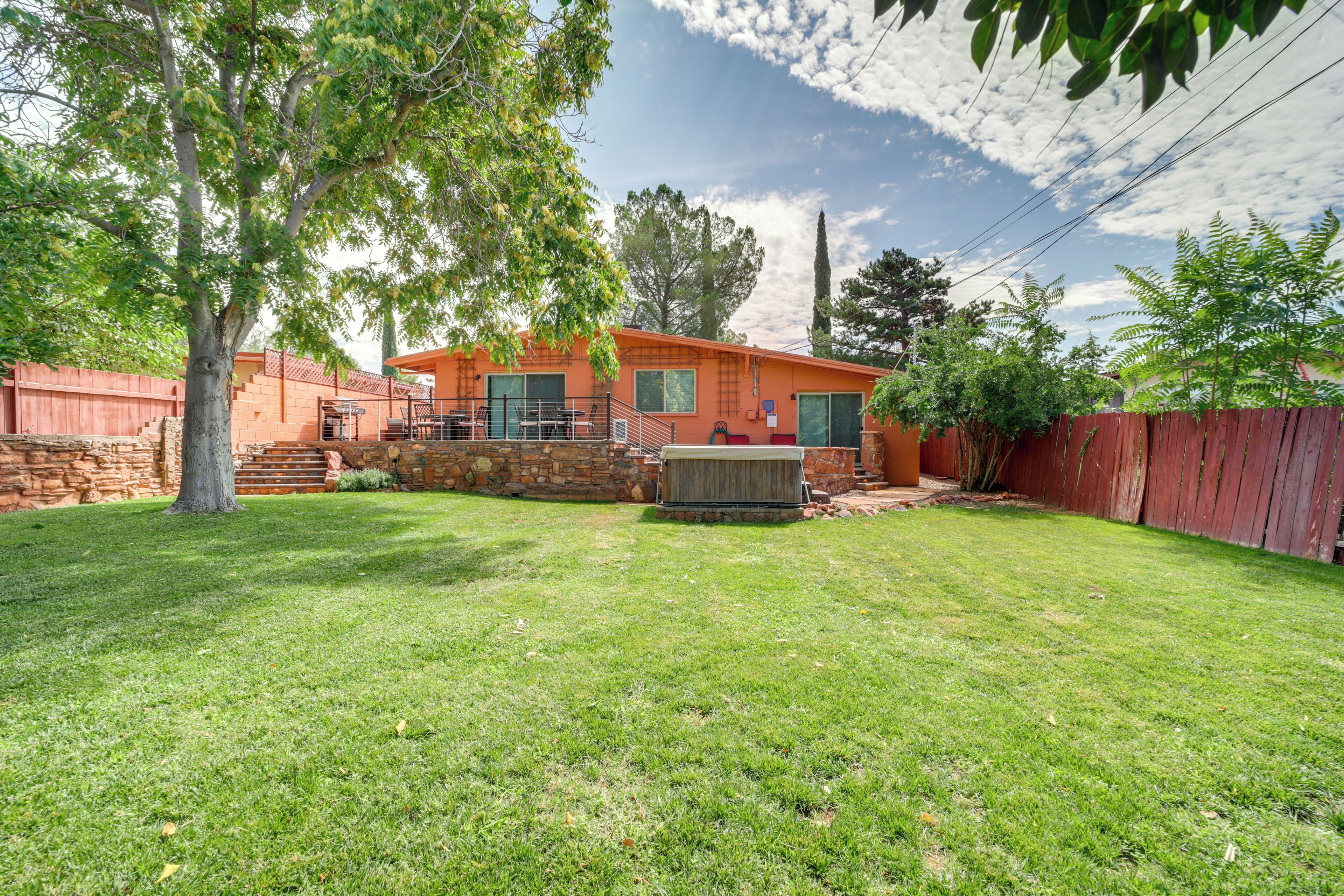 A house with a stone foundation, a red wooden fence, and a well-maintained lawn.