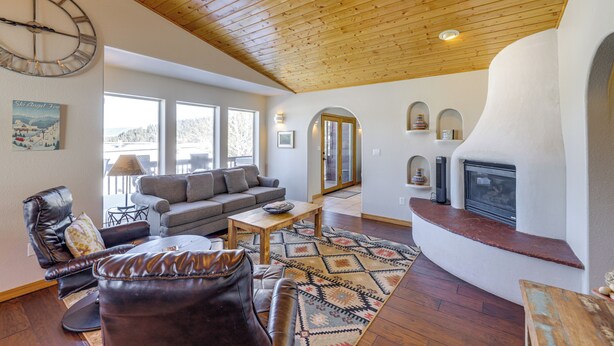 A cozy living room with a wooden ceiling, a fireplace, a sofa, a leather chair, and a patterned rug. - Angel Fire Townhome w/ Hot Tub: 2 Mi to Ski Resort (Angel Fire)