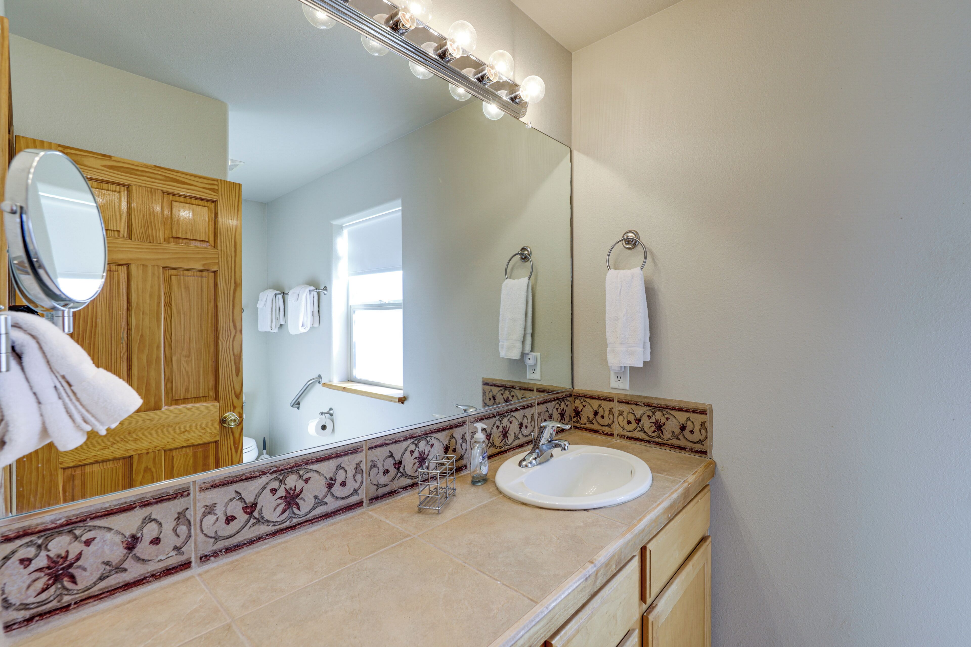 Ein Badezimmer mit Holztür, Waschbecken mit Spiegel darüber und einem Waschtisch mit Handtuchhalter.