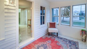 A room with a red patterned rug, a white bench, and a window with a view of a tree and a building. - Michigan Retreat w/ Screened-in Porch, Near Lakes! (Belleville)