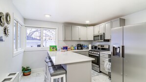 A modern kitchen with white cabinets, stainless steel appliances, and a central island with bar stools. - Michigan Retreat w/ Screened-in Porch, Near Lakes! (Belleville)