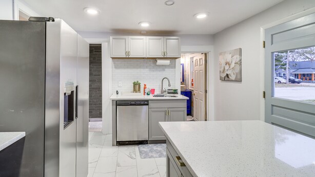 A modern kitchen with stainless steel appliances, white cabinetry, and a large window providing a view of the street. - Michigan Retreat w/ Screened-in Porch, Near Lakes! (Belleville)