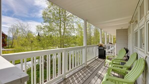 Ein überdachter Balkon mit weißer Reling, grünen Adirondack-Stühlen und einem Grill.