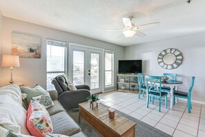 A living room with a sofa, coffee table, and chairs, a television, and a ceiling fan.