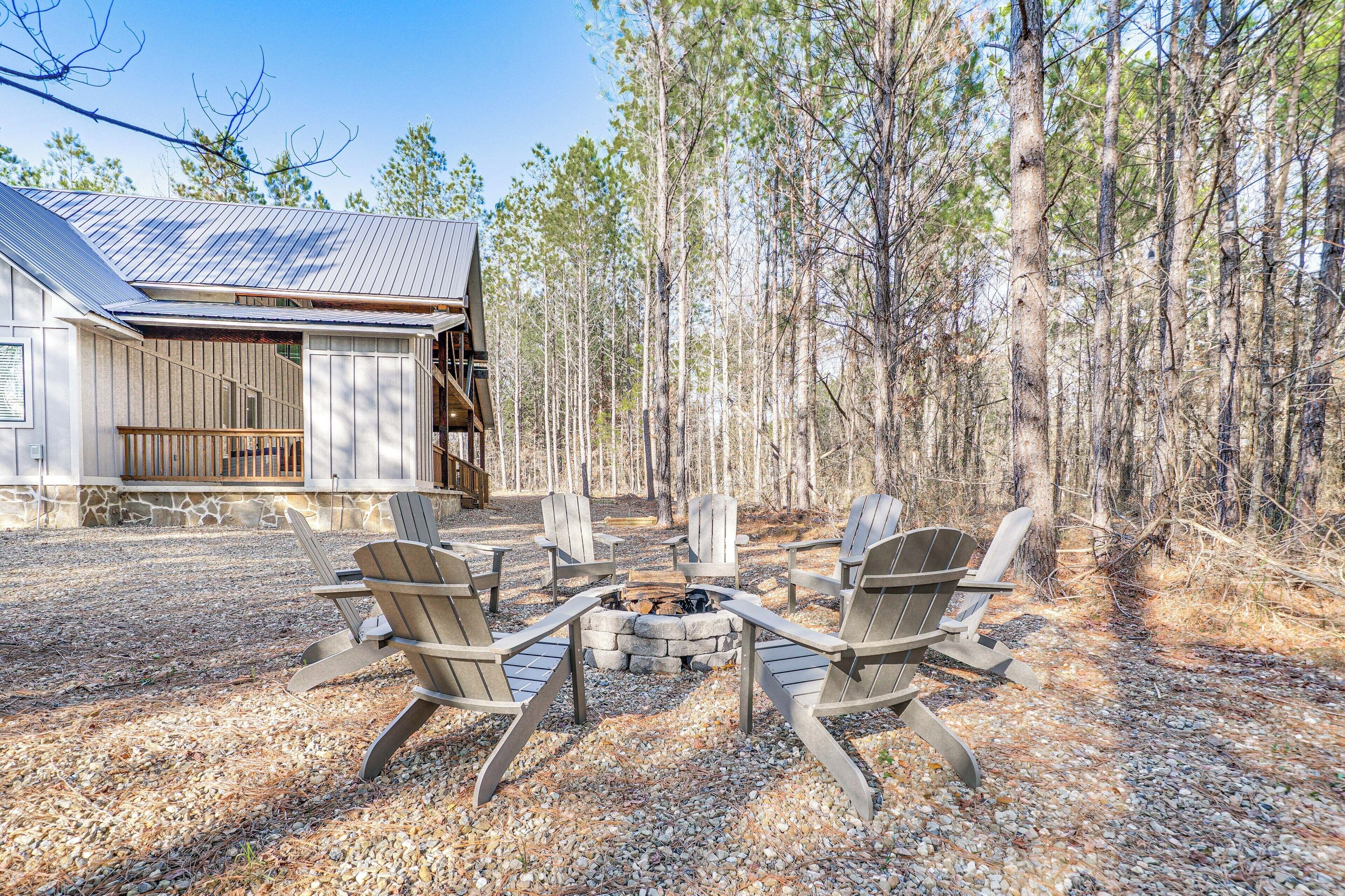 A cabin with a stone fire pit surrounded by Adirondack chairs, set in a forested area.