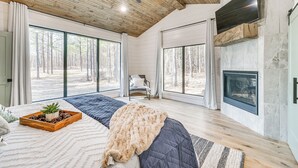 Ein geräumiges Schlafzimmer mit einem großen Bett, einem Kamin und Blick auf den Wald durch große Fenster.