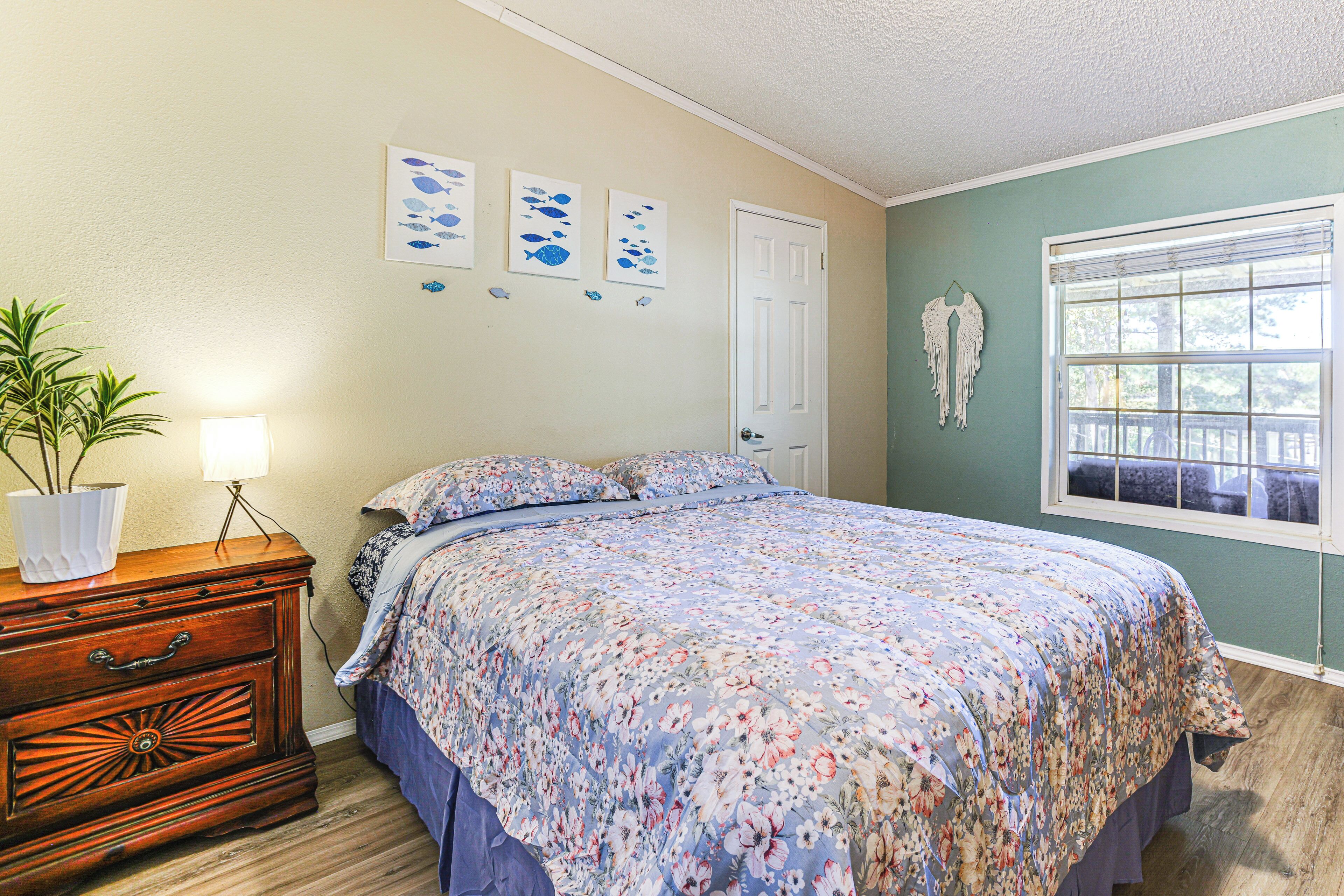 Un dormitorio con colcha estampada, cómoda con cajones, planta en maceta y decoración en la pared.