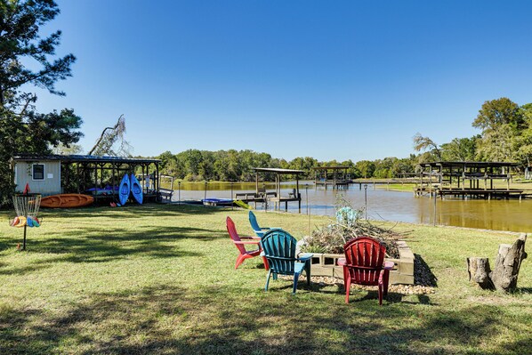 A lakeside area with chairs, kayaks, and a small cabin. - Lake Livingston Home w/ Dock & Deck! (Huntsville)