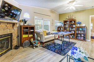 Uma sala de estar com lareira, sofá, mesa de bilhar e estante de livros.