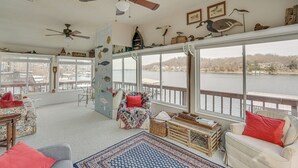 A cozy living room with a view of a lake, featuring a ceiling fan, a large window, and a variety of decorative items. - Private Dock: Lake of the Ozarks Hideaway! (Sunrise Beach)