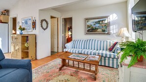 Un salon avec un canapé à rayures, une table basse en bois, un fauteuil bleu et une plante en pot.