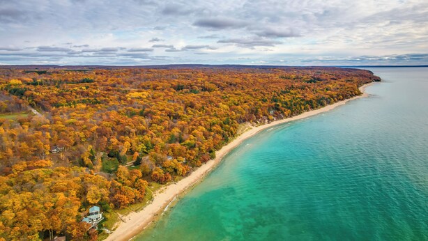 An aerial view of a coastal area with a beach, dense forest, and a clear view of the ocean. - 17 Mi to Skiing! Lake-view Michigan Home w/ Deck (Harbor Springs)