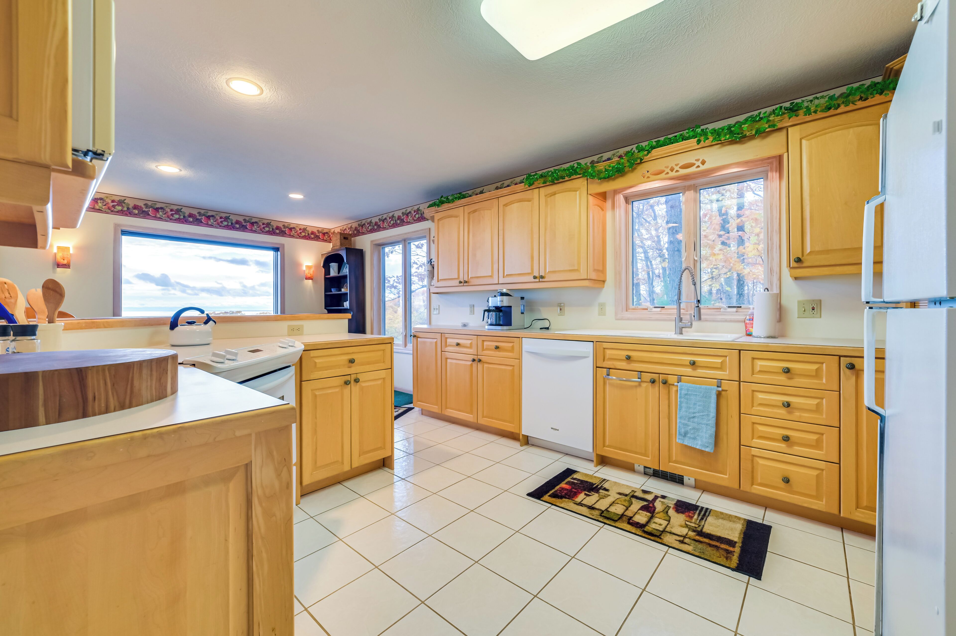 Una cocina moderna con armarios de madera, un refrigerador blanco y una ventana con vista a árboles.