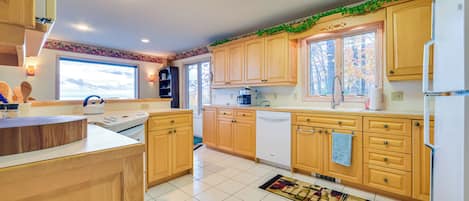 Una cocina moderna con armarios de madera, un refrigerador blanco y una ventana con vista a árboles.