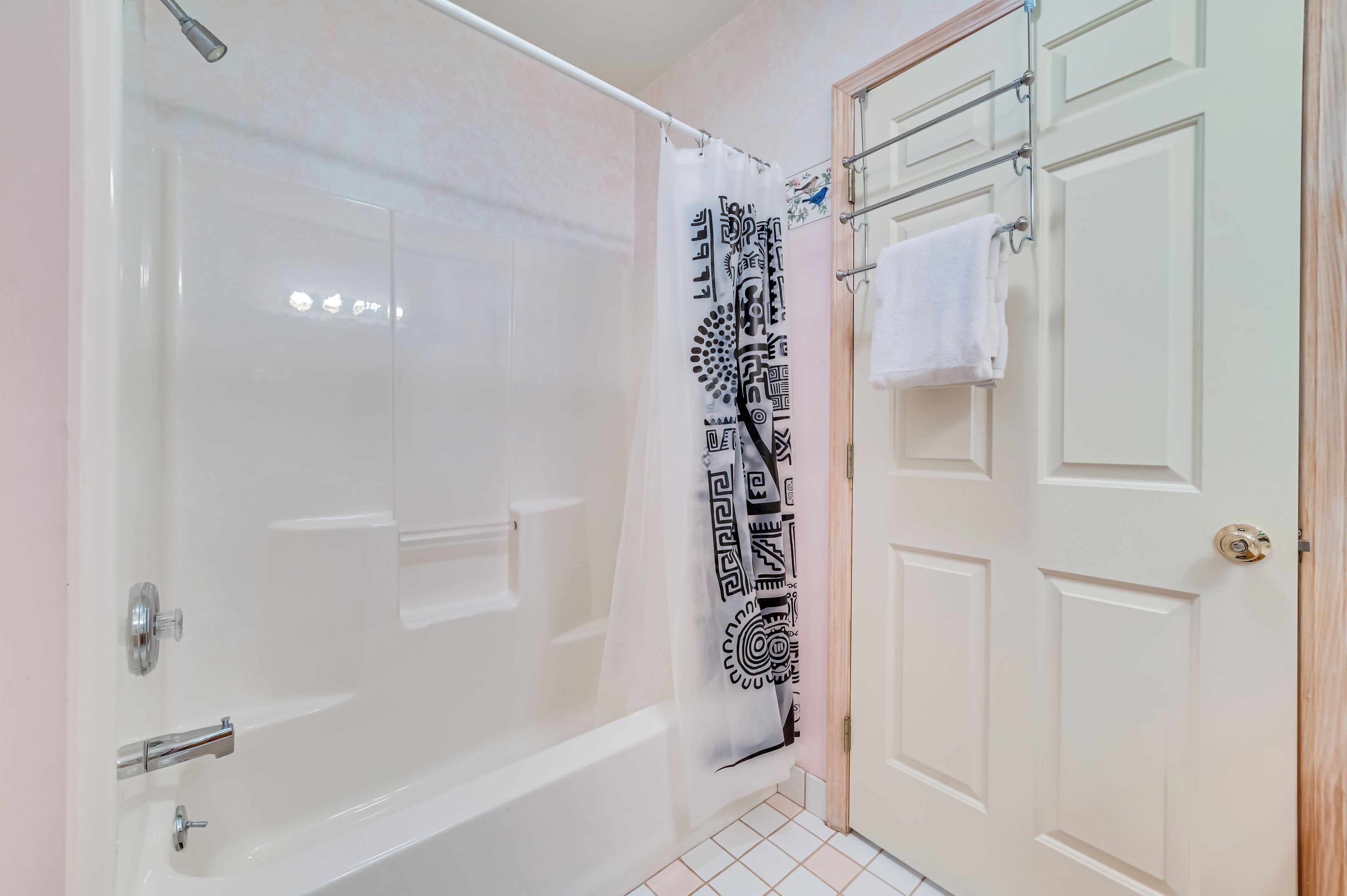 Un baño con una bañera blanca, una cortina de ducha con diseño geométrico y una toalla blanca colgada en un perchero.