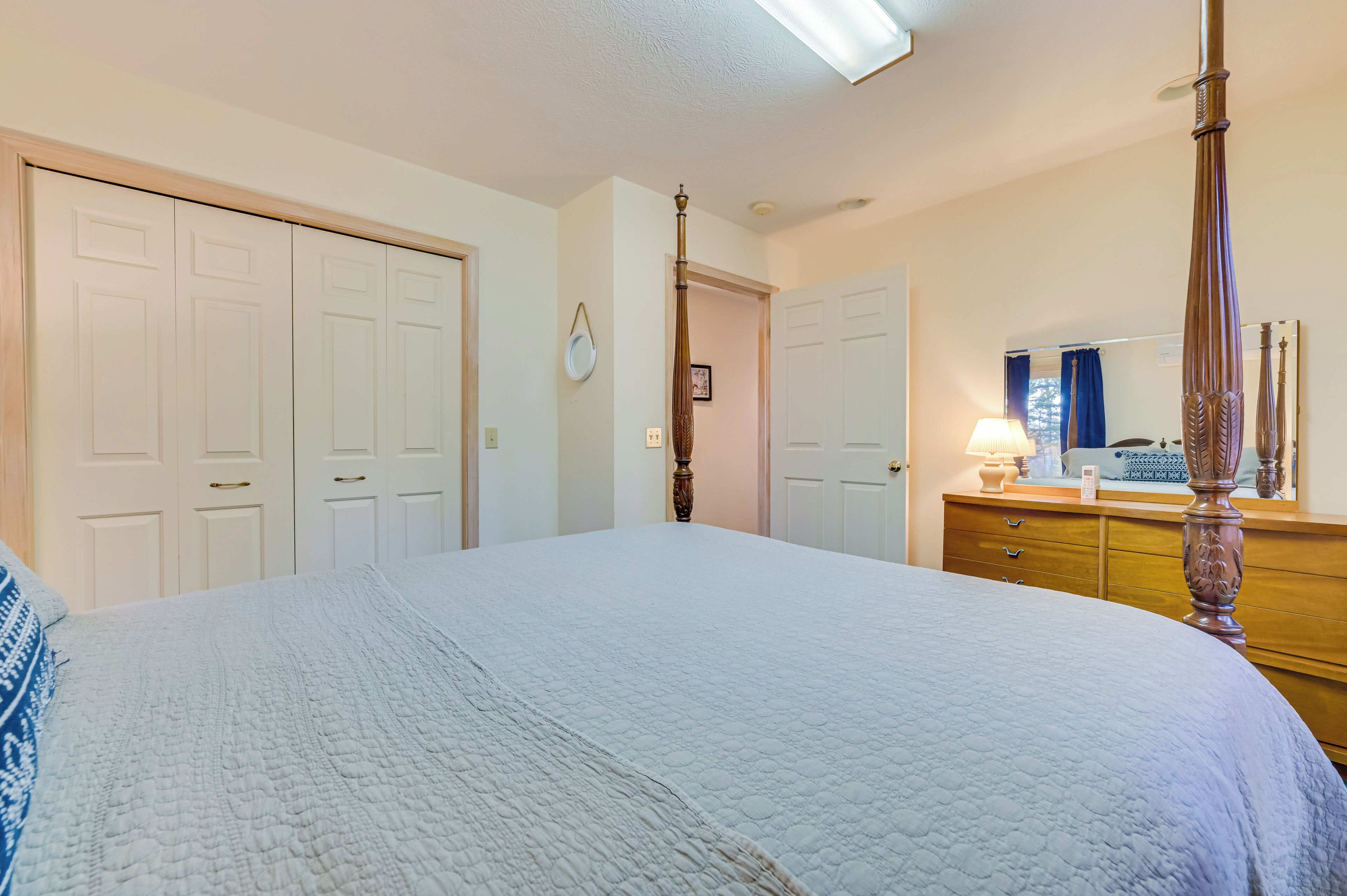 Ein Schlafzimmer mit einem großen Bett, einer hölzernen Kommode, einem Spiegel und einer Tür zu einem weiteren Raum.