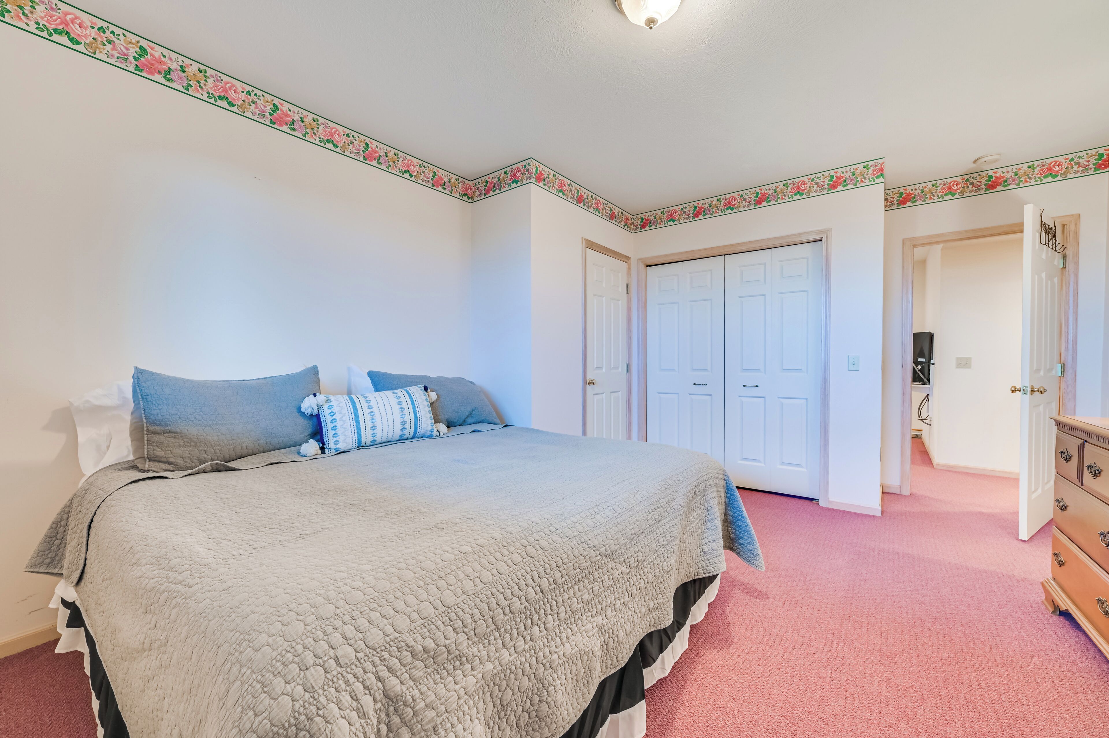 Une chambre à coucher avec un grand lit, une commode et une porte donnant sur une autre pièce.