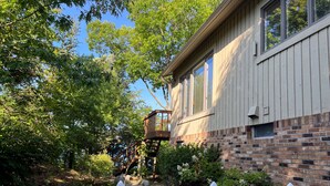 A wooden house with a brick foundation, a white picket fence, and a wooden pathway leading to a wooden deck. - Sunset Landing - Private Sandy Beach, Lamkin Drive 3 BD, 2 BATH (Sleeps 6) (Harbor Springs)