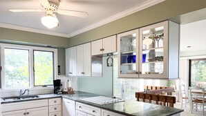 A kitchen with white cabinets, a granite countertop, a ceiling fan, and a dining area with a wooden table and chairs. - Sunset Landing - Private Sandy Beach, Lamkin Drive 3 BD, 2 BATH (Sleeps 6) (Harbor Springs)