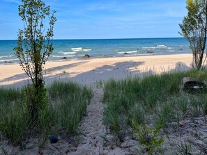 Ein Strand mit einem sandigen Pfad, der zum Wasser führt, umgeben von Gras und kleinen Bäumen.