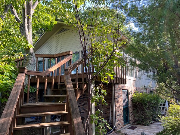 Eine Holztreppe führt zu einem Haus mit Ziegelaußenwand und großen Fenstern.