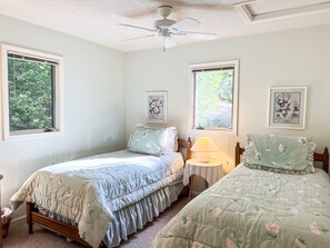A bedroom with two beds, a ceiling fan, and two windows with floral artwork.