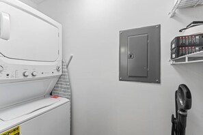 A laundry room with a washing machine, a utility room with a door, and a hairdryer on a shelf.